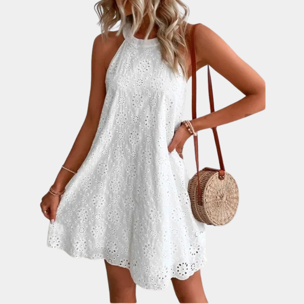 Vrouw in witte kanten zomerjurk met halternek, draagt een ronde rieten tas. Perfect voor casual zomermode en stranduitjes.