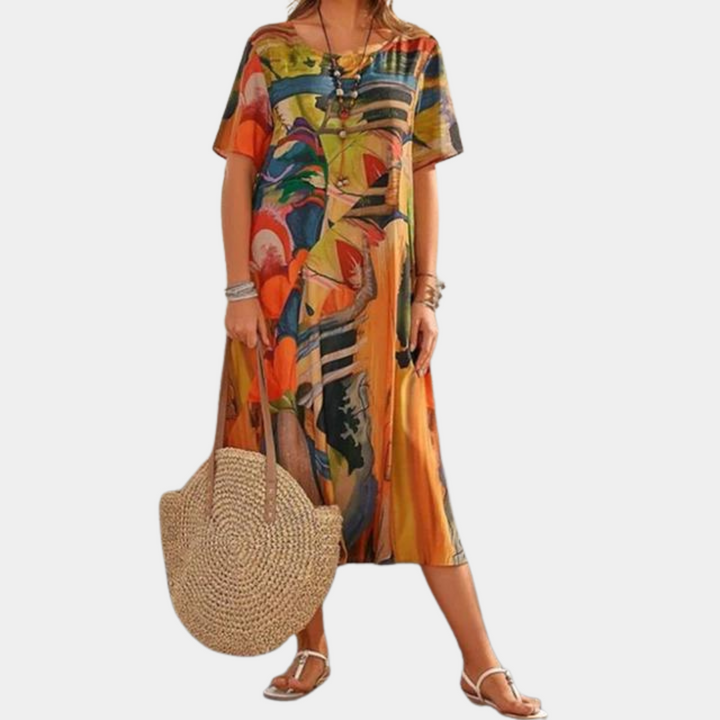 Vrouw in kleurrijke, bloemenprint zomerjurk met korte mouwen, draagt een grote strooien tas en sandalen. Perfect voor strandmode en zomerse stijl.