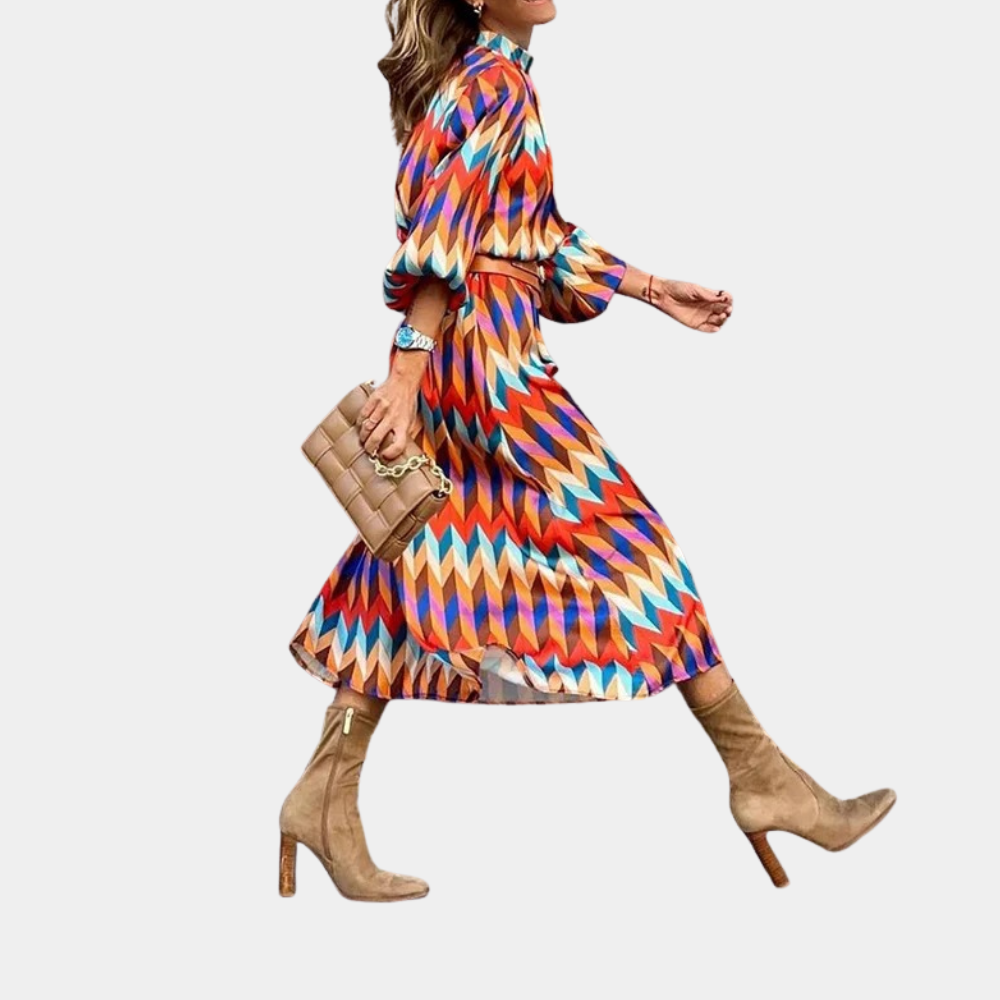 Vrouw in kleurrijke zigzag jurk met lange mouwen, bruine laarzen en beige handtas. Modieuze outfit, trendy damesmode, herfststijl.
