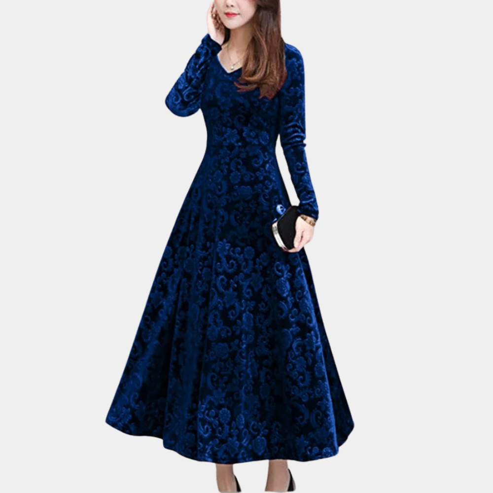 Donkerblauwe fluwelen jurk met lange mouwen en elegant patroon, perfect voor avondkleding. Vrouw draagt zwarte clutch. Stijlvolle damesmode.