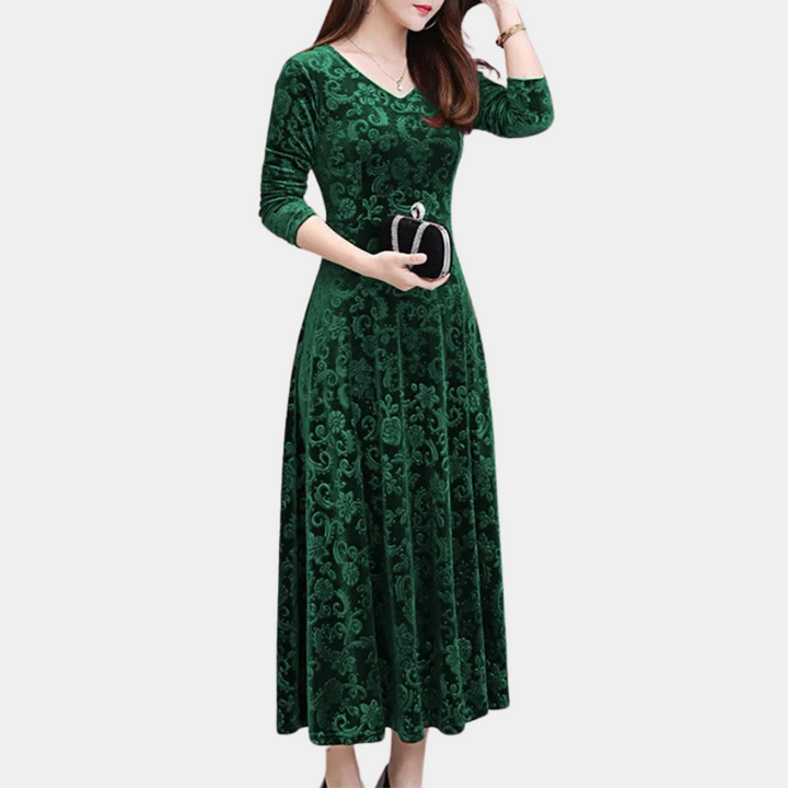Groene fluwelen jurk met lange mouwen en sierlijk patroon, gedragen door vrouw met handtas. Elegante avondjurk voor speciale gelegenheden.