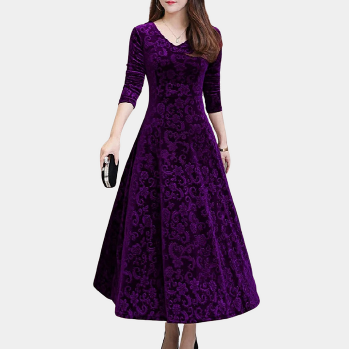 Paarse fluwelen jurk met lange mouwen en elegante patronen, perfect voor avondkleding. Vrouw draagt zwarte clutch. Ideaal voor formele gelegenheden.