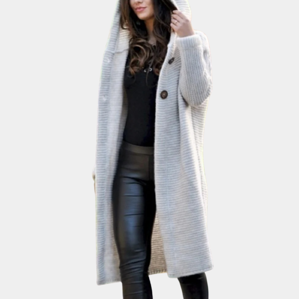Vrouw in lange beige gebreide jas met capuchon, zwarte leren broek en zwarte top. Modieuze herfst- of winterkleding. Stijlvolle damesmode.