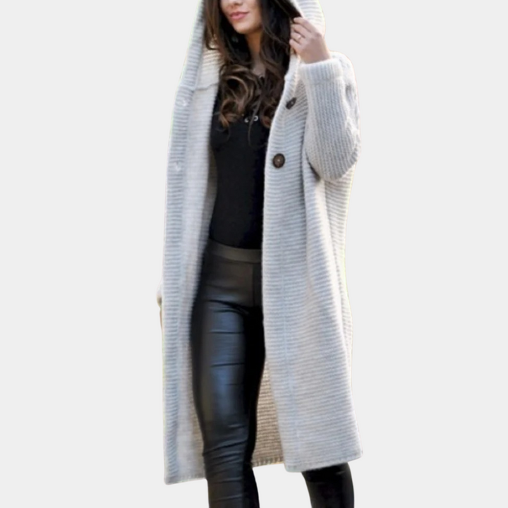 Vrouw in lange beige gebreide jas met capuchon, zwarte leren broek en zwarte top. Modieuze herfst- of winterkleding. Stijlvolle damesmode.