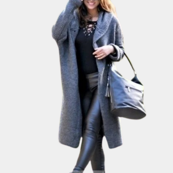 Vrouw in grijze gebreide lange jas, zwarte leren broek en zwarte tas. Modieuze herfstkleding, casual stijl, trendy damesmode.