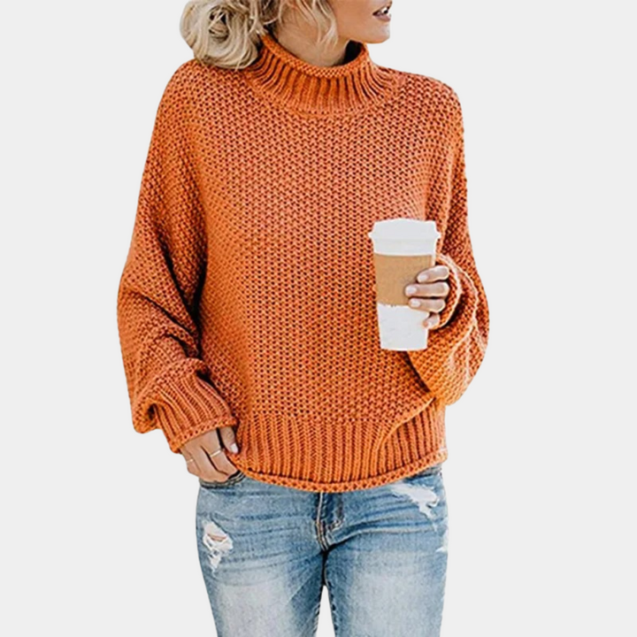 Oranje gebreide trui met col, gedragen door persoon met blond haar, gecombineerd met blauwe spijkerbroek en koffiebeker. Modieuze herfstkleding.
