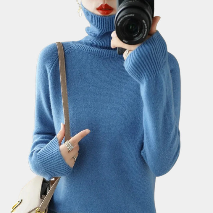 Vrouw in blauwe coltrui met camera en beige schoudertas. Stijlvolle wintermode, trendy dameskleding, casual look.