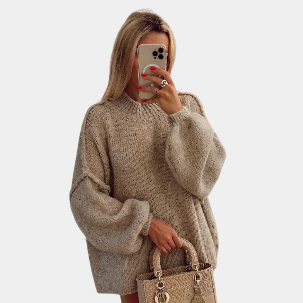 Vrouw in oversized beige trui met ballonmouwen, houdt een beige handtas vast en maakt een selfie met smartphone. Modetrend herfst 2023.