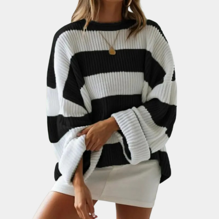 Vrouw draagt zwart-wit gestreepte oversized trui, ribgebreid, met ronde hals. Modieuze dameskleding, herfst-winter stijl, casual outfit.