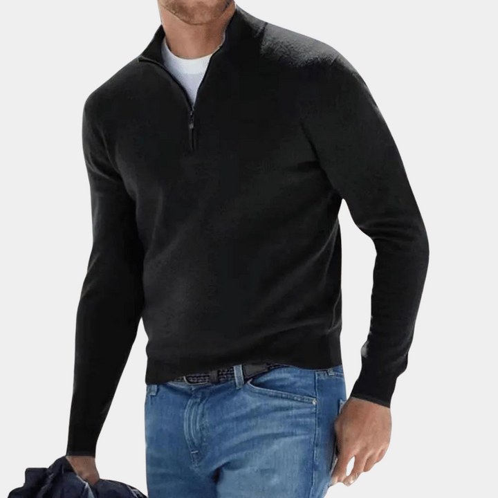 Zwarte herentrui met halve rits, gedragen door model in blauwe jeans. Stijlvolle casual outfit, perfect voor herfst- en wintermode.