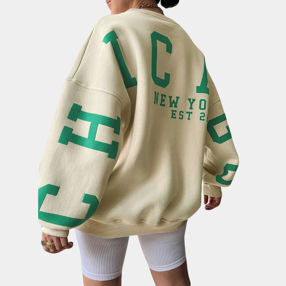 Beige oversized sweatshirt met groene "Chicago" en "New York Est 2" opdruk, gedragen door model. Trendy streetwear, casual mode.
