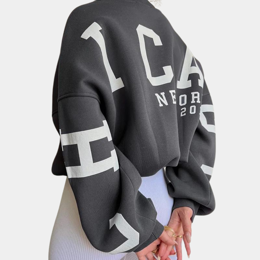 Donkergrijze oversized sweater met witte letters "ICA" en "NORD 2020", gedragen door model. Trendy streetwear, casual mode, comfortabele pasvorm.
