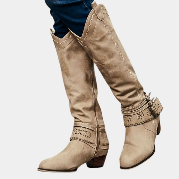 Beige suède cowboylaarzen met decoratieve stiksels en gespen, lage hak, gedragen door persoon in blauwe jeans. Trendy damesmode, westerse stijl.