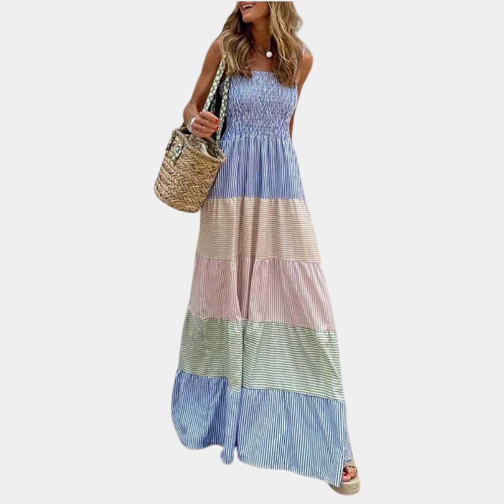Vrouw in lange, gestreepte zomerjurk met blauwe, roze en groene tinten, draagt een rieten tas. Perfecte boho-stijl voor zomermode.