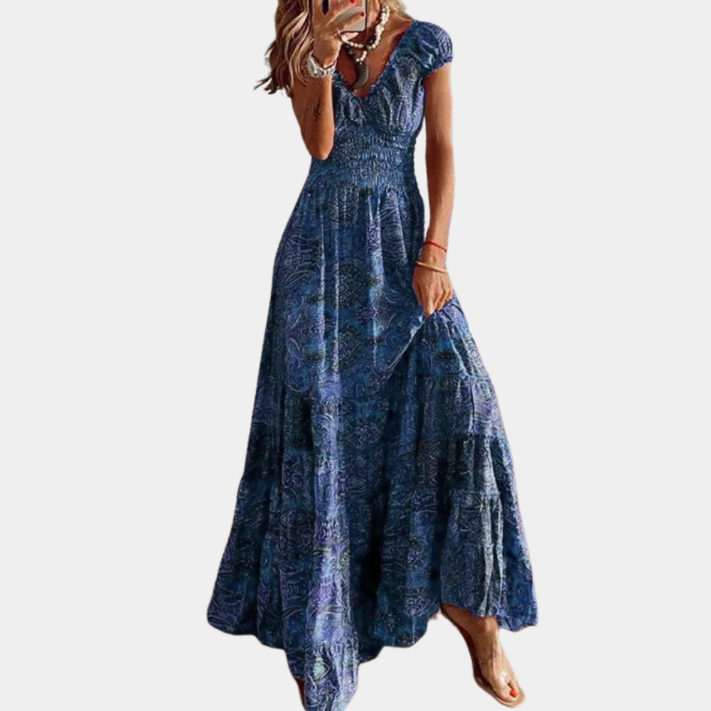 Vrouw in lange blauwe bohemian jurk met korte mouwen en V-hals, gemaakt van luchtige stof. Perfect voor zomerse dagen en casual evenementen.