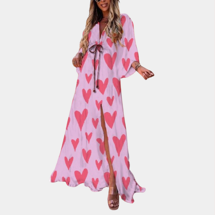 Vrouw in roze maxi-jurk met hartjesprint, lange mouwen en ceintuur. Perfect voor zomermode, casual en elegante stijl.