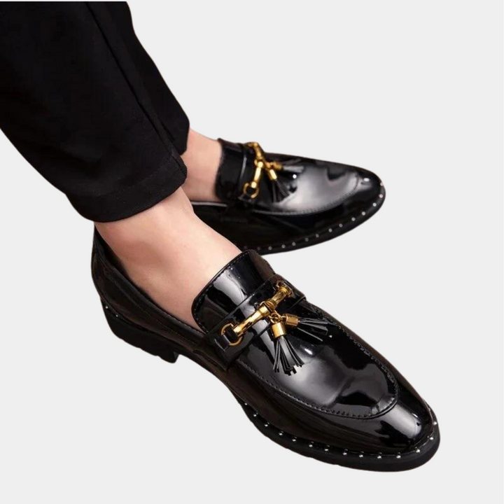 Zwarte leren loafers met gouden details en kwastjes, gedragen door een persoon. Stijlvolle herenschoenen, glanzend design, geschikt voor formele gelegenheden.