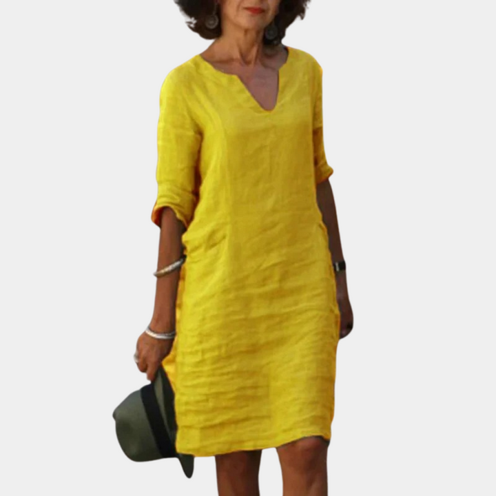 Vrouw in gele linnen jurk met V-hals en driekwartsmouwen, casual zomeroutfit, modeaccessoires, witte achtergrond.