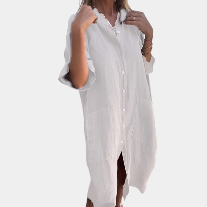 Vrouw draagt witte linnen overhemdjurk met knopen, driekwart mouwen en losse pasvorm. Perfect voor casual zomeroutfits en strandkleding.