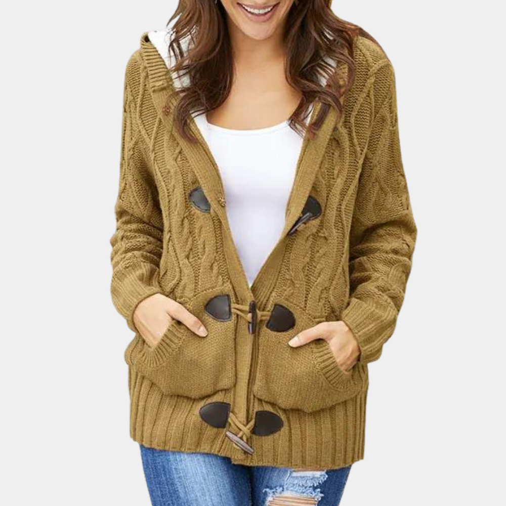 Vrouw draagt bruine kabelgebreide trui met houtje-touwtje sluiting, witte top en blauwe jeans. Stijlvolle herfstmode, casual dameskleding.