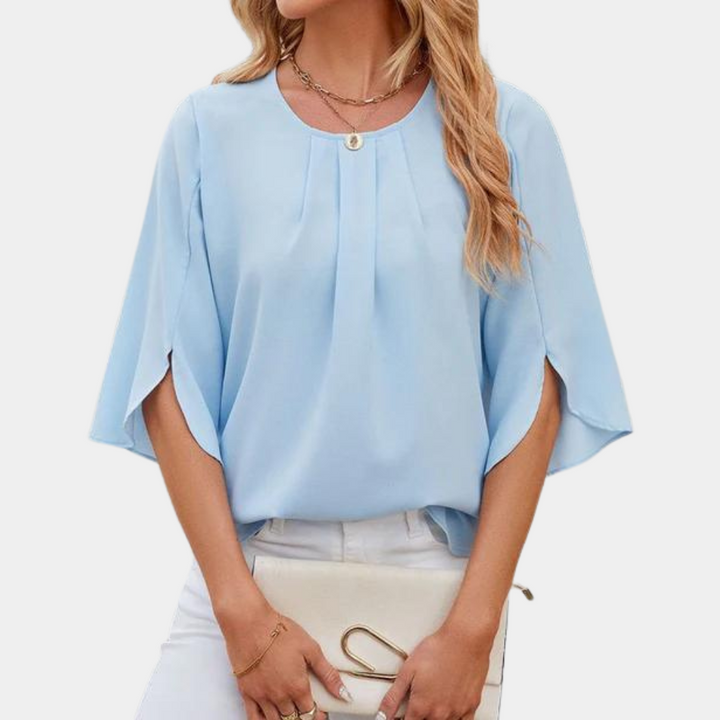 Vrouw in lichtblauwe blouse met wijde mouwen en ronde hals, draagt een witte tas. Modieuze dameskleding, casual stijl, elegante uitstraling.