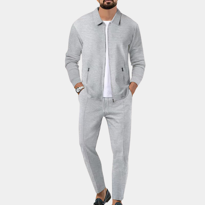 Grijs heren joggingpak, bestaande uit een jas en broek, ideaal voor casual en sportieve gelegenheden. Comfortabel en stijlvol ontwerp.