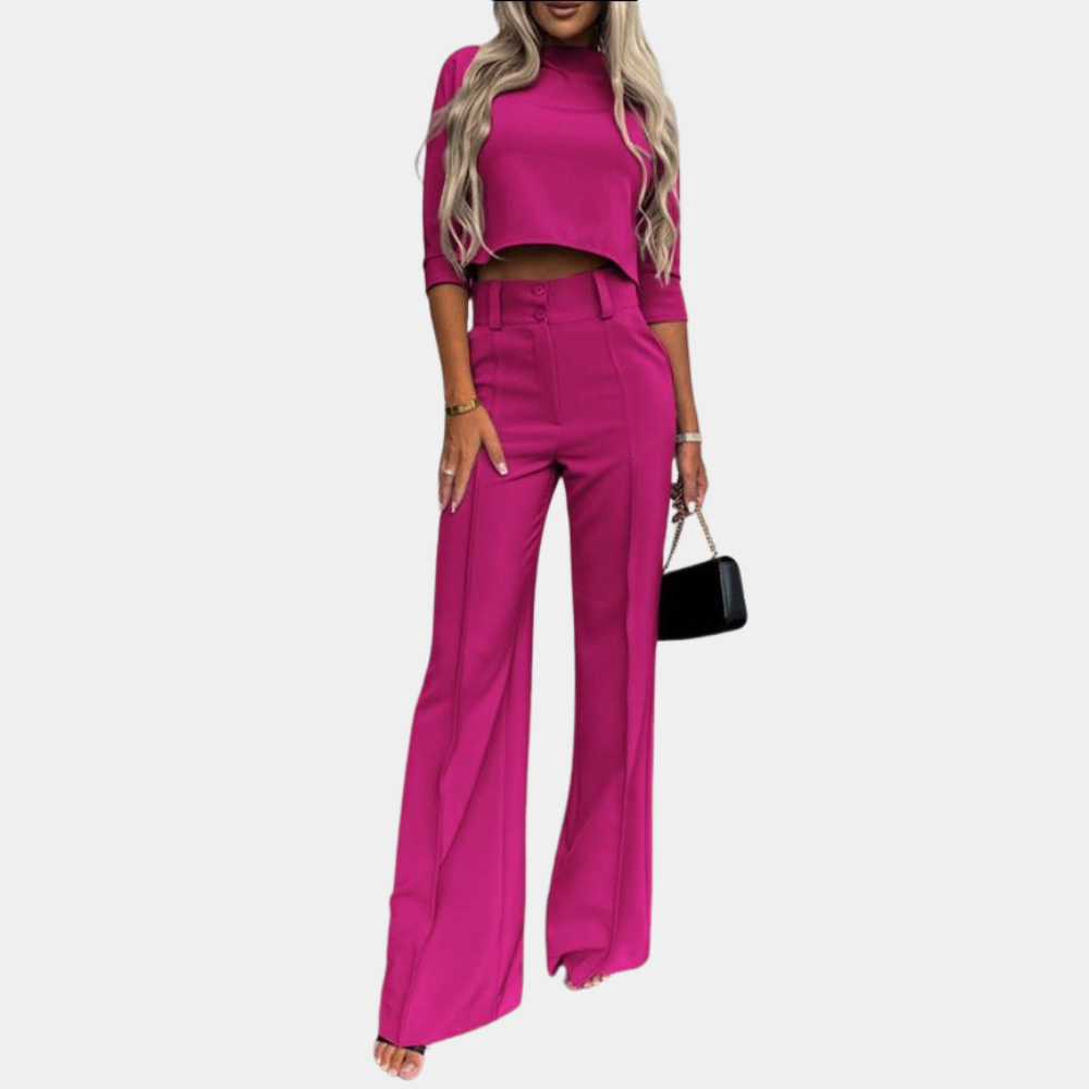 Vrouw in felroze tweedelig pak met wijde broek en crop top, draagt een zwarte handtas. Modieuze dameskleding, trendy outfit.