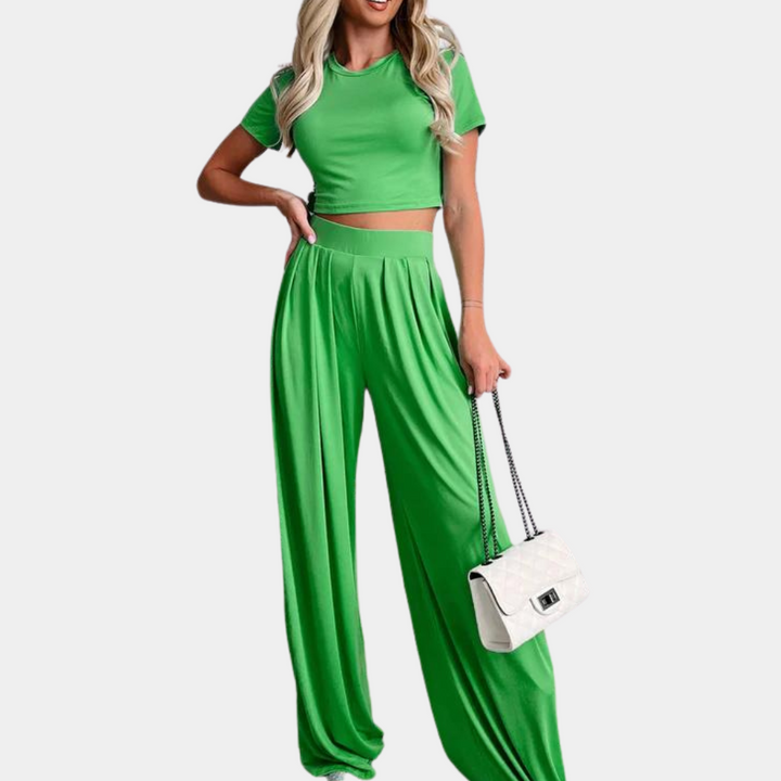 Vrouw in groene crop top en wijde broek, trendy zomeroutfit, met witte handtas. Modieuze dameskleding, casual stijl, comfortabele pasvorm.