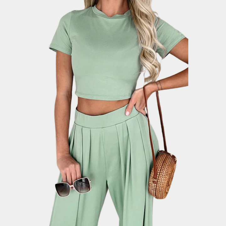 Lichtgroene damesoutfit met korte mouwen en hoge taille broek, gecombineerd met een ronde rieten tas en zonnebril. Trendy zomerlook.