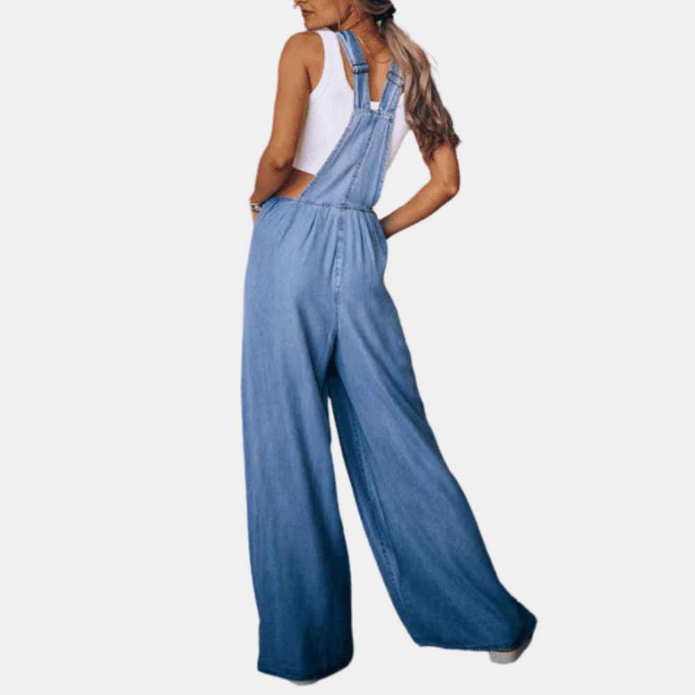Vrouw in blauwe denim jumpsuit met wijde pijpen, witte tanktop. Modieuze dameskleding, casual stijl, comfortabele pasvorm.