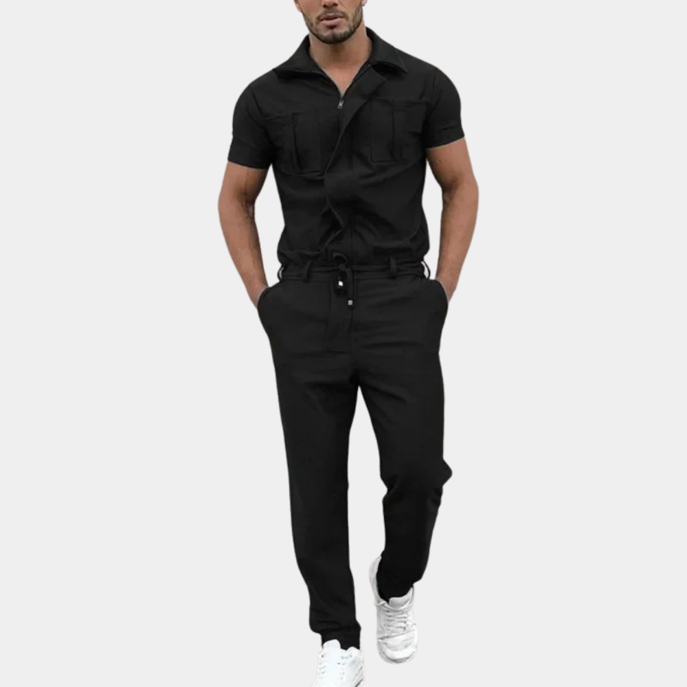 Zwarte heren jumpsuit met korte mouwen, borstzakken en knoopsluiting, gedragen door een man met witte sneakers. Stijlvolle en moderne herenkleding.
