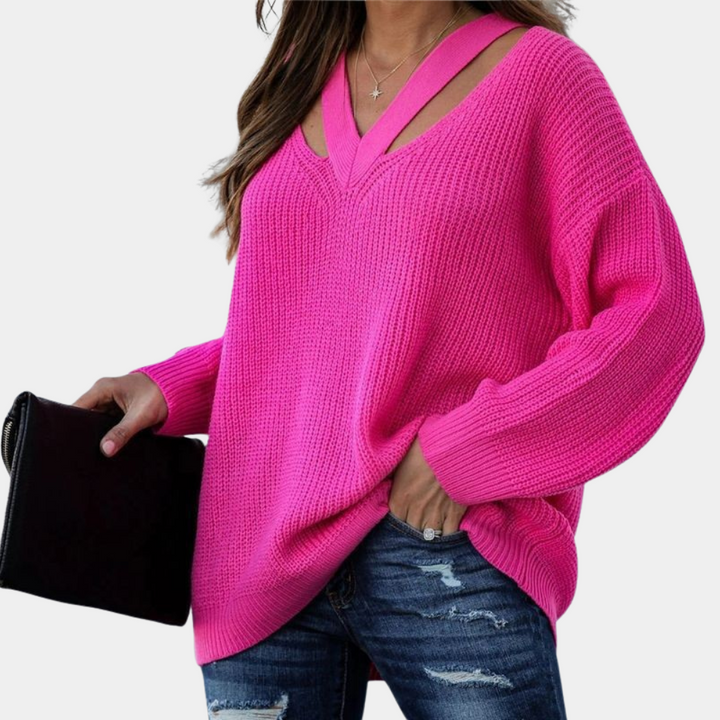Vrouw in felroze trui met V-hals en lange mouwen, gecombineerd met gescheurde jeans en zwarte clutch. Modieuze dameskleding, casual stijl.