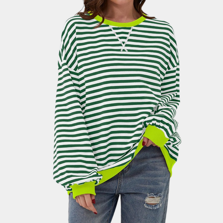 Groen-wit gestreepte trui met lange mouwen, ronde hals en neon groene accenten, gedragen door een model in blauwe jeans. Modieuze dameskleding.
