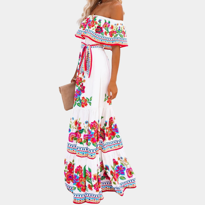 Witte off-shoulder maxi-jurk met kleurrijke bloemenprint, boho-stijl, zomermode, vrouw draagt bruine clutch, casual elegantie.