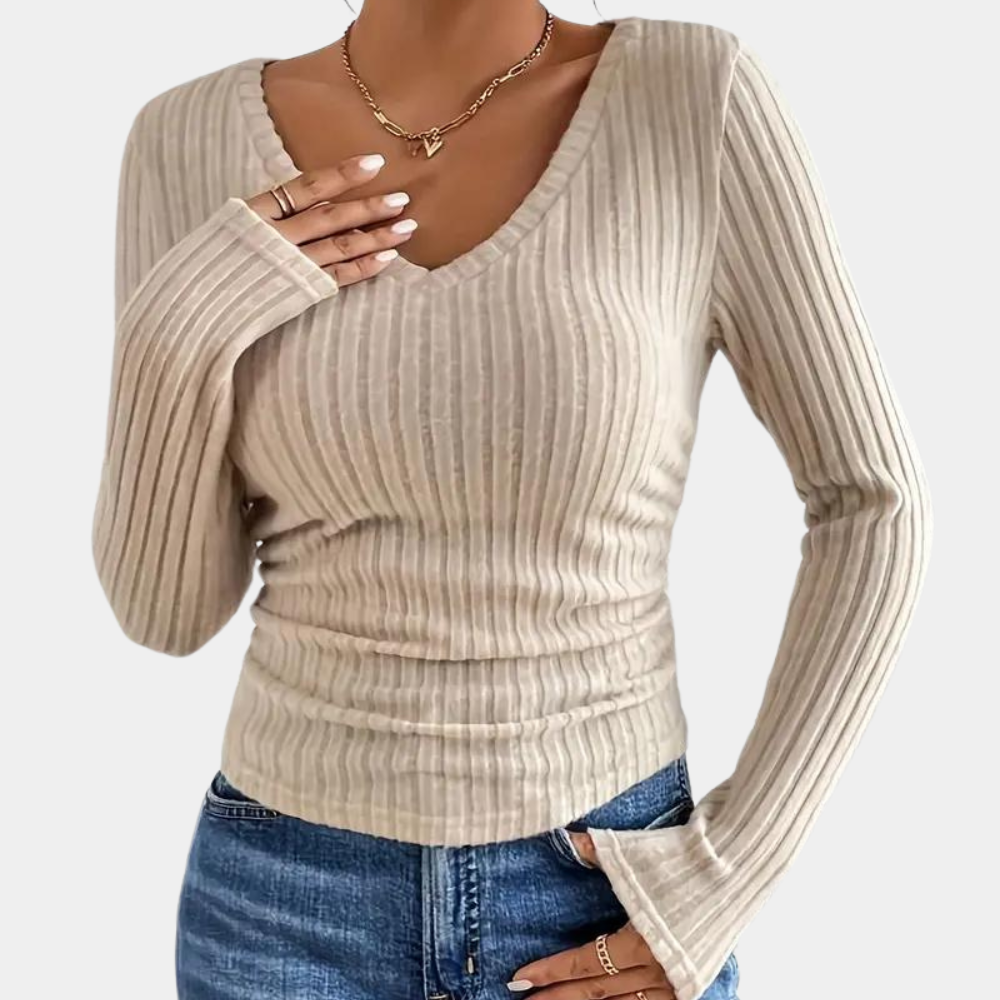 Vrouw draagt beige geribbelde trui met V-hals en lange mouwen, gecombineerd met blauwe jeans. Modieuze dameskleding, casual stijl.