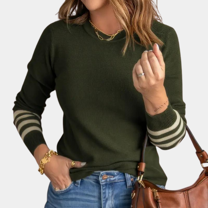 Vrouw in legergroene trui met gestreepte mouwen, gouden sieraden en bruine handtas. Modieuze dameskleding, casual herfstoutfit.