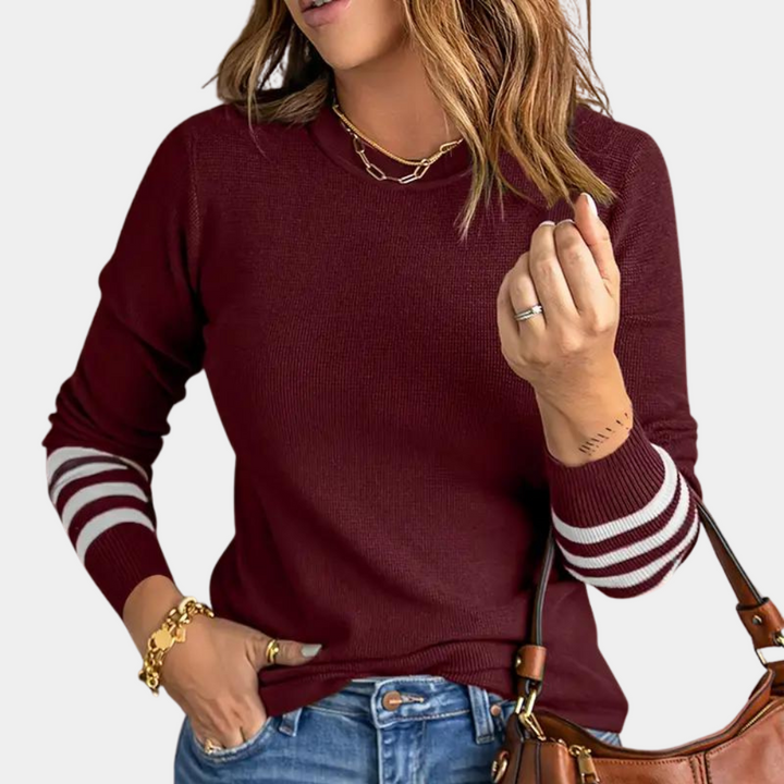 Vrouw in bordeauxrode trui met witte strepen op mouwen, gouden sieraden en blauwe jeans. Modieuze herfstkleding, casual stijl.