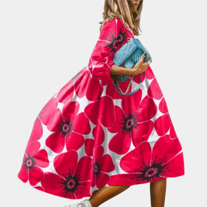 Vrouw in roze jurk met grote bloemenprint, draagt blauwe handtas. Modieuze zomerjurk, casual stijl, opvallend design. Perfect voor zomerse dagen.