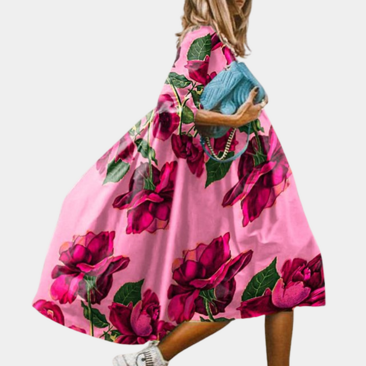 Vrouw in roze jurk met grote rode rozenprint, draagt blauwe handtas. Modieuze zomerjurk, bloemenpatroon, casual stijl.