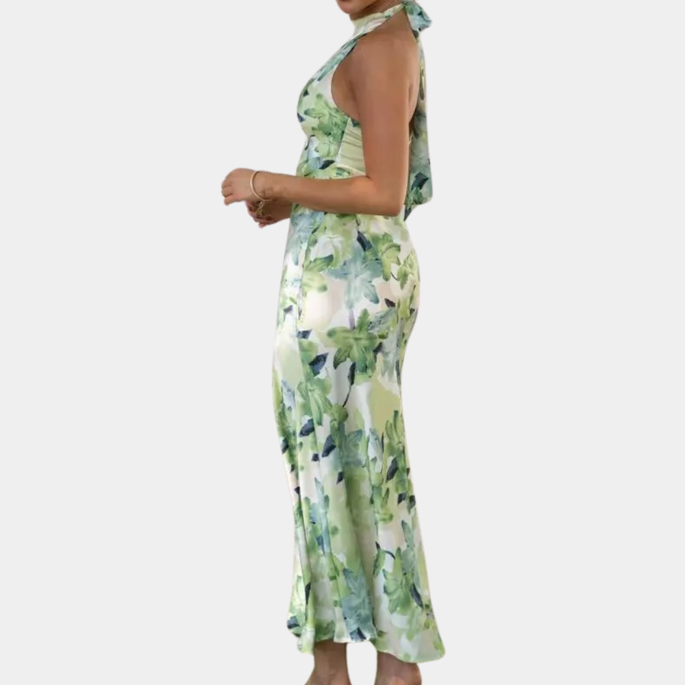 Vrouw in groene bloemenjurk, halternek, zijaanzicht. Elegante zomerjurk, casual mode, trendy dameskleding, perfecte pasvorm.