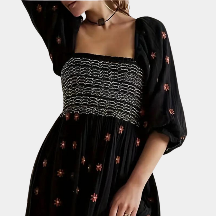 Zwarte boho-jurk met bloemenprint en gesmokte taille, lange mouwen en vierkante halslijn. Perfect voor casual en stijlvolle gelegenheden.