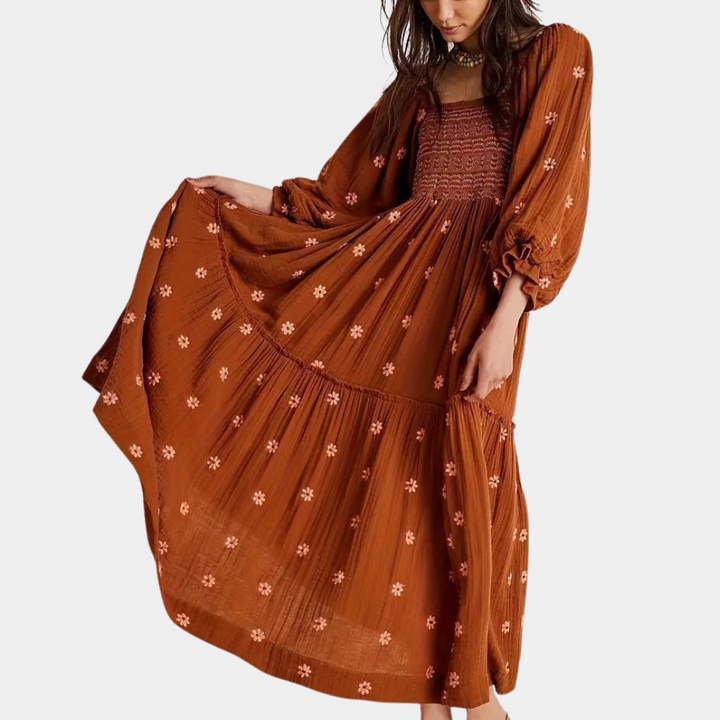 Vrouw in lange, lichtbruine boho-jurk met bloemenprint en pofmouwen. Trendy damesmode, bohemian stijl, casual zomeroutfit.
