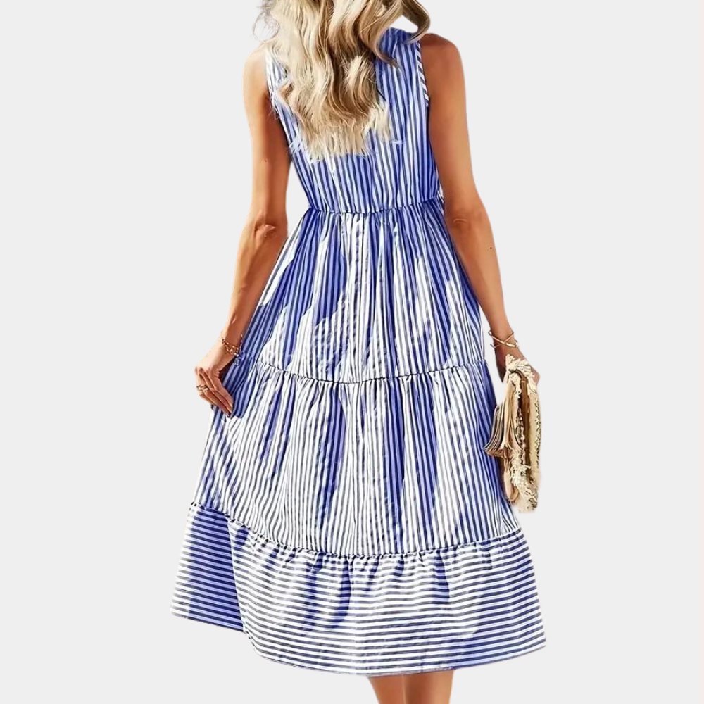 Vrouw in lichtblauwe gestreepte zomerjurk, mouwloos en knielang, met golvende rok. Perfect voor casual en strandoutfits.