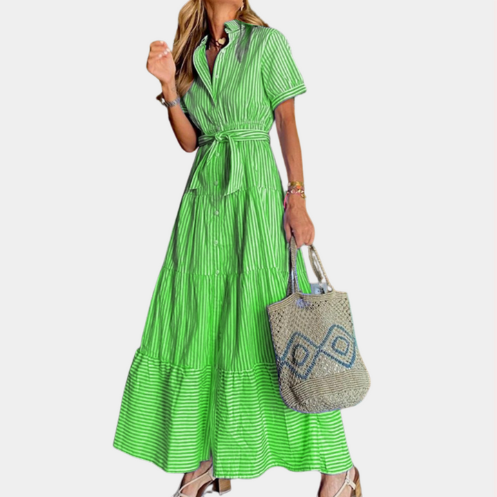 Vrouw in groene gestreepte maxi-jurk met ceintuur, draagt een geweven tas. Zomermode, casual elegantie, dameskleding.