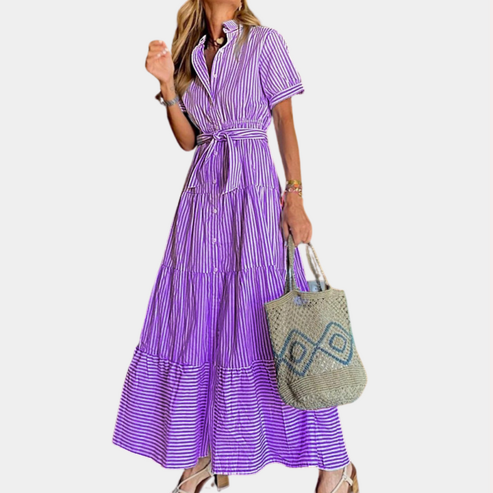 Vrouw in lange paarse gestreepte jurk met ceintuur, draagt een geweven tas. Stijlvolle zomeroutfit, modetrend, casual elegantie.