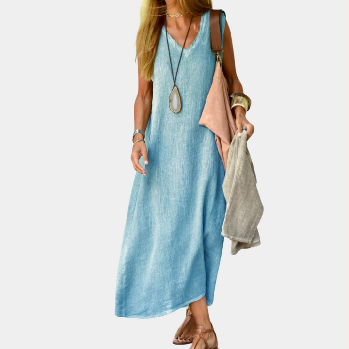 Vrouw in blauwe linnen jurk met lange ketting, draagt beige sandalen en houdt stoffen tas vast. Zomerjurk, casual mode, dameskleding.