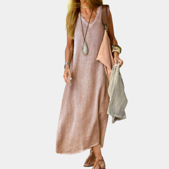 Vrouw in roze linnen maxi-jurk met lange ketting en sandalen, draagt tas en sjaal. Zomermode, casual dameskleding, boho-stijl.