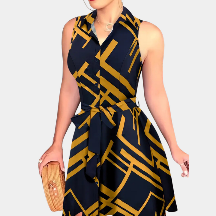 Zwarte mouwloze jurk met geometrisch goud patroon, knoopsluiting en strikceintuur. Vrouw houdt een rieten clutch. Elegante damesmode.
