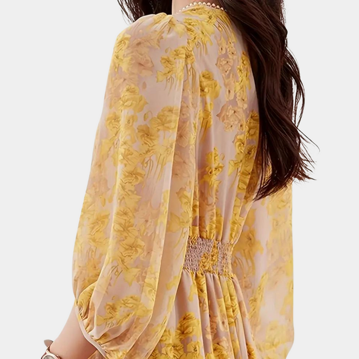 Vrouw in gele bloemenjurk met lange mouwen, elegante plooien en elastische tailleband. Perfect voor zomermode en casual chique stijl.