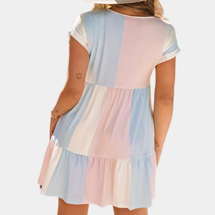 Vrouw in zomerse jurk met pastelblauwe, roze en witte blokken, korte mouwen en ronde hals. Perfect voor casual zomeroutfits.